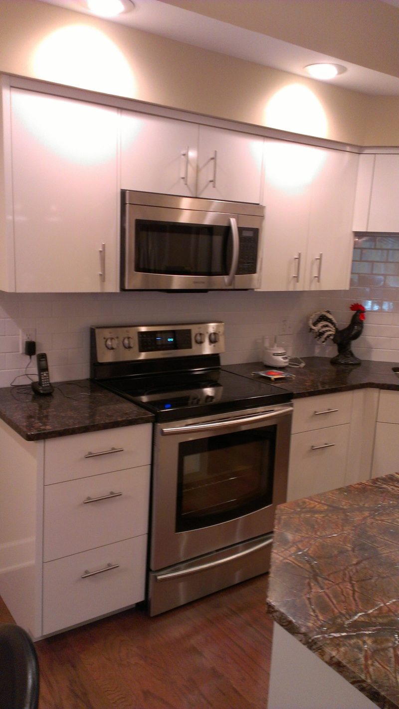White cabinets with a stainless range and microwave beside a granite island
