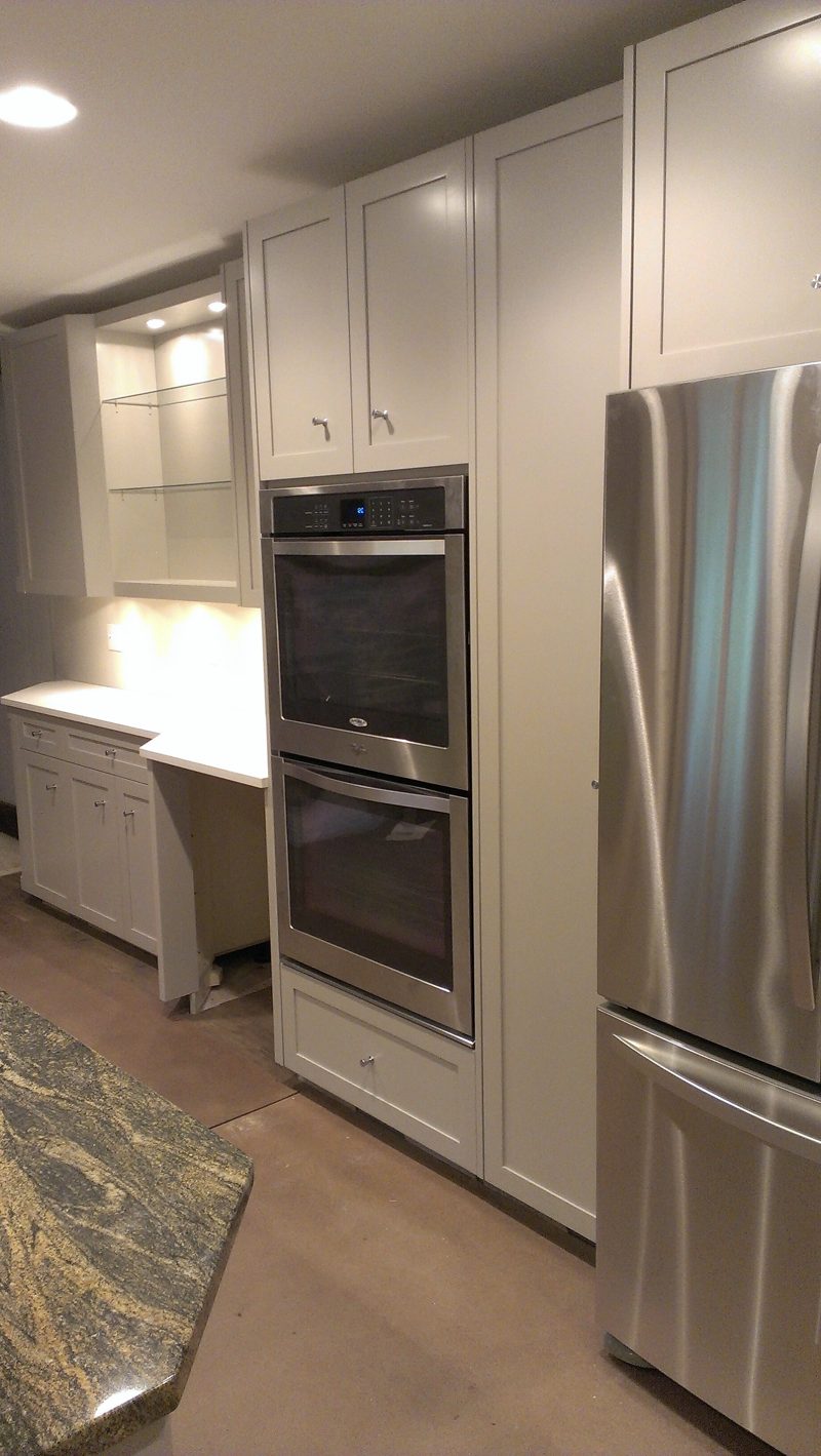 Tall gray cabinets with double wall ovens beside a stainless refrigerator