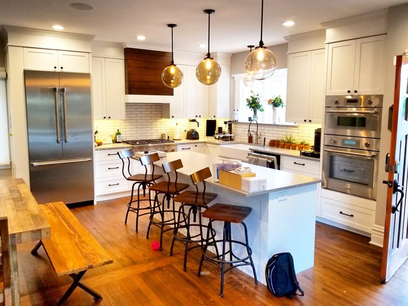 White kitchen with walnut accents, brass pendants, and a stool-lined island