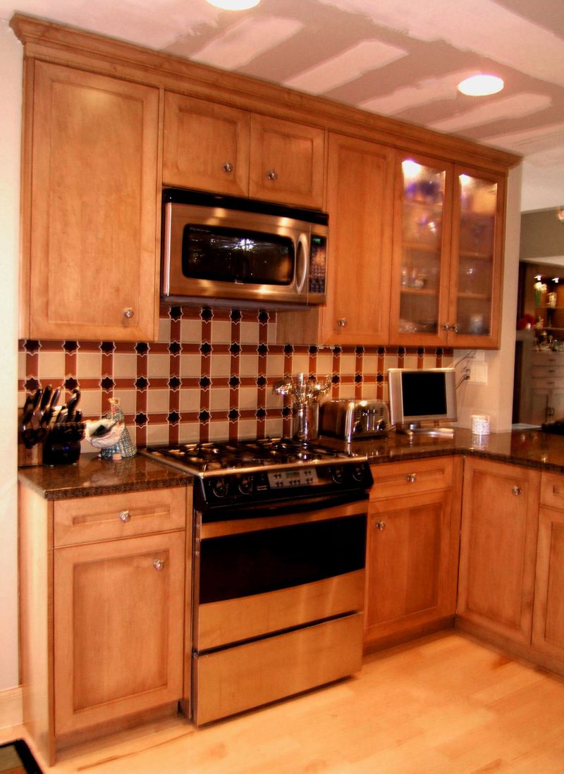 Maple cabinetry with a gas range, microwave, and dark tile backsplash