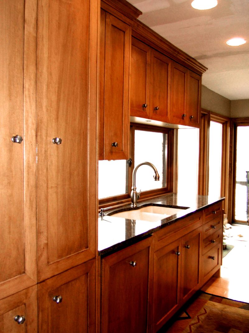 Tall maple cabinets beside a sink window with granite counters