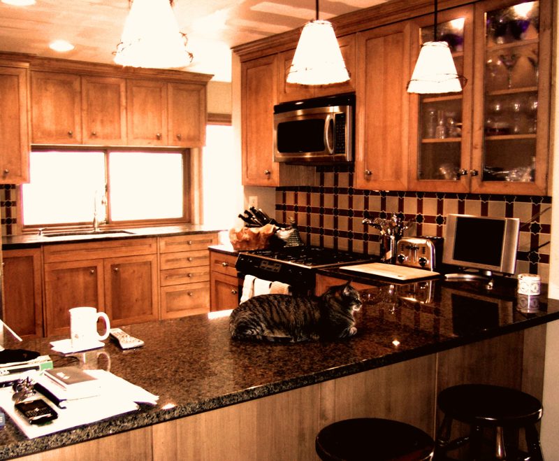 Maple kitchen with a granite peninsula, bell pendants, and dark tile backsplash