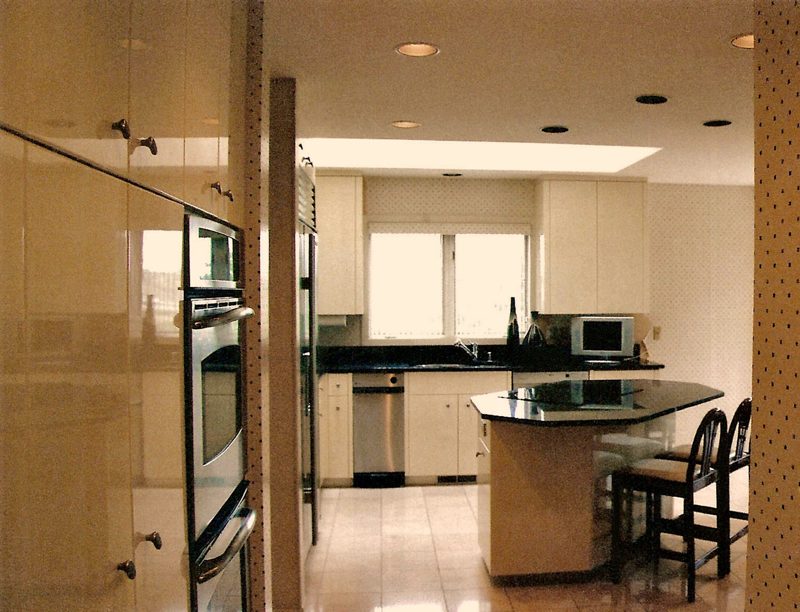 Light-colored kitchen cabinetry and center island with dark countertops and built-in ovens