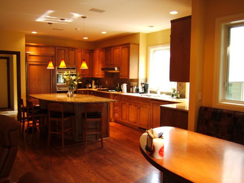 Wood kitchen with an oval island and pendant lights, seen from the dining table