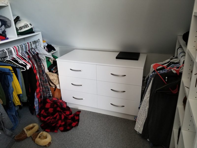 White dresser with four drawers in a closet with hanging clothes
