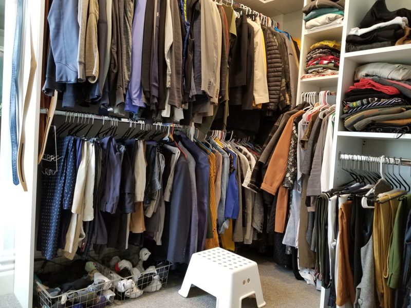 White closet system with hanging rods and shelves full of clothes