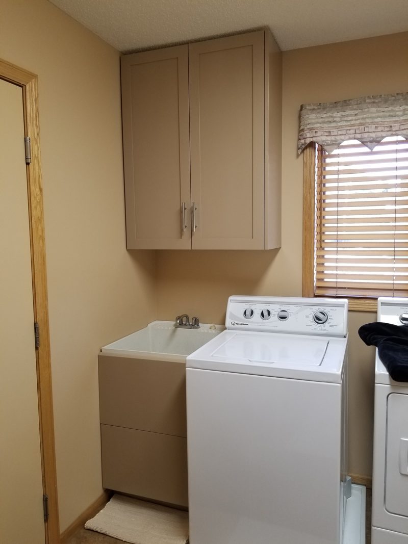 Taupe upper cabinet over a laundry sink beside a washer