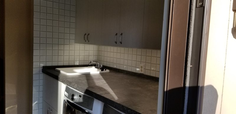 Dark laundry countertop with a sink below taupe upper cabinets