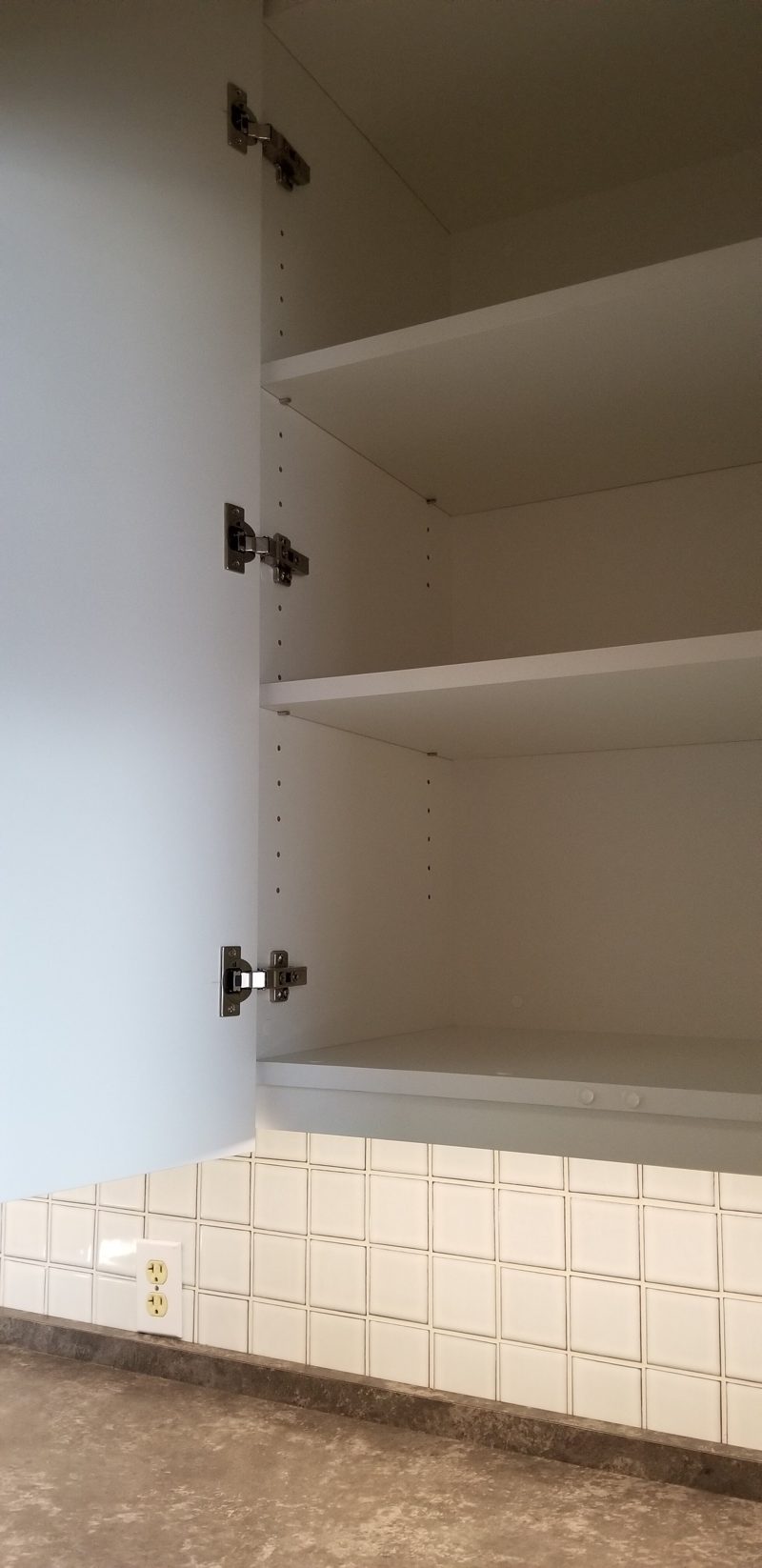 Open upper cabinet with adjustable shelves above a tiled backsplash
