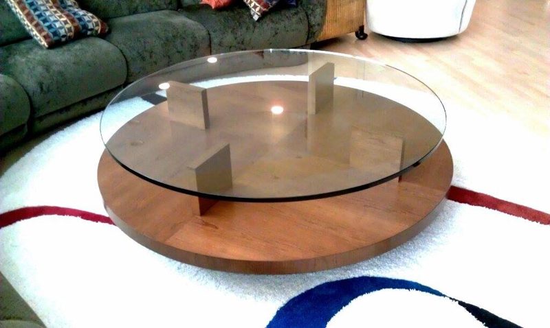 Round glass coffee table on a wood base with crossed wood supports