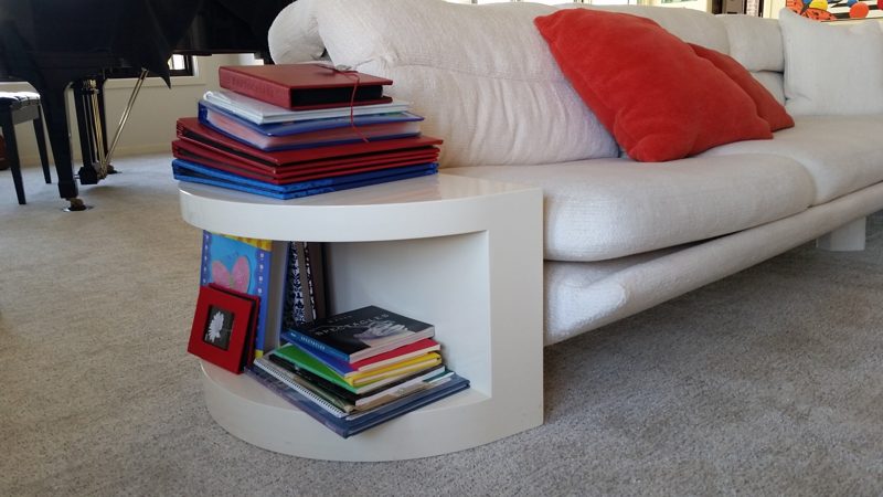 White round end table with book storage beside a white sofa
