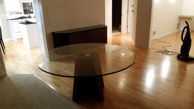 Round glass dining table on a dark wood base beside a sideboard