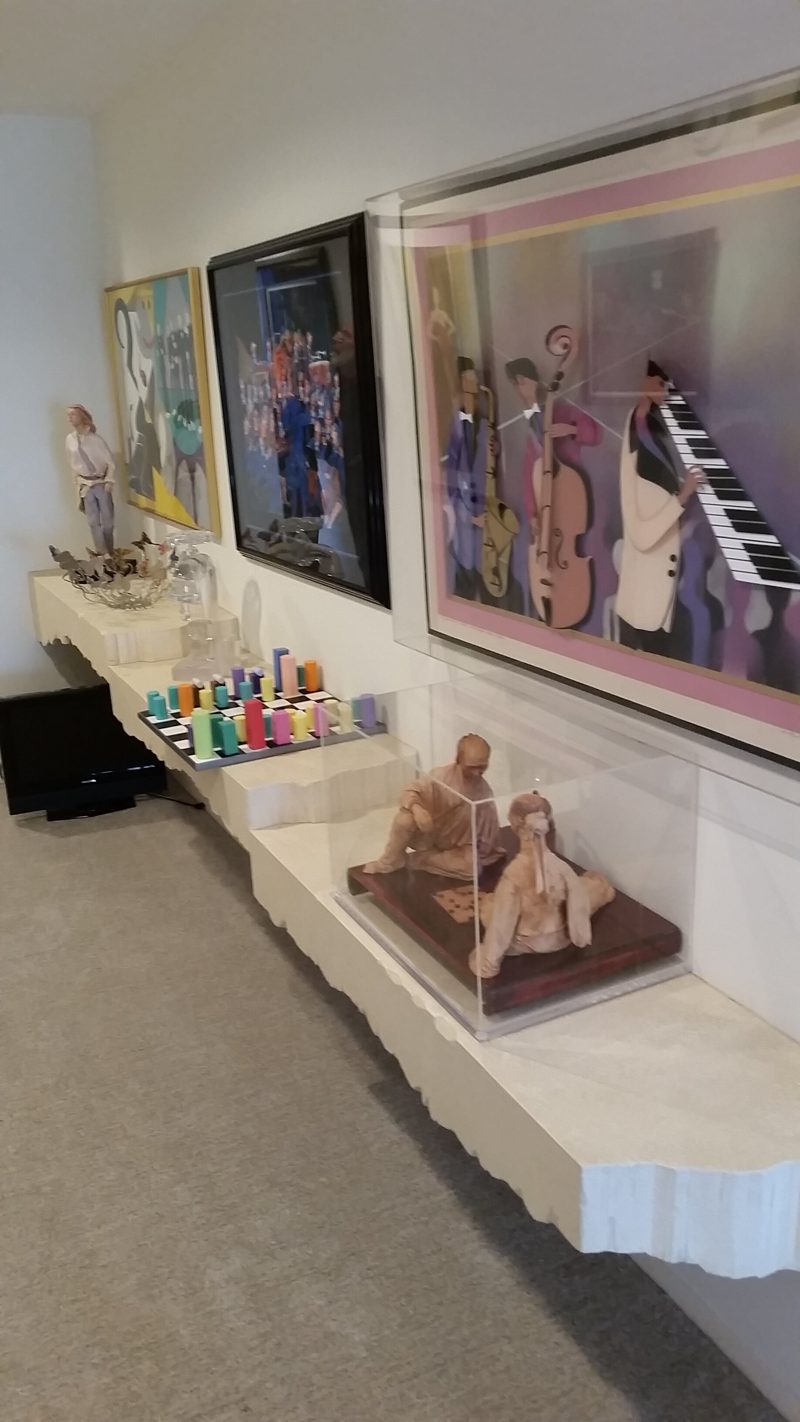 Long white floating shelf displaying sculptures below framed artwork