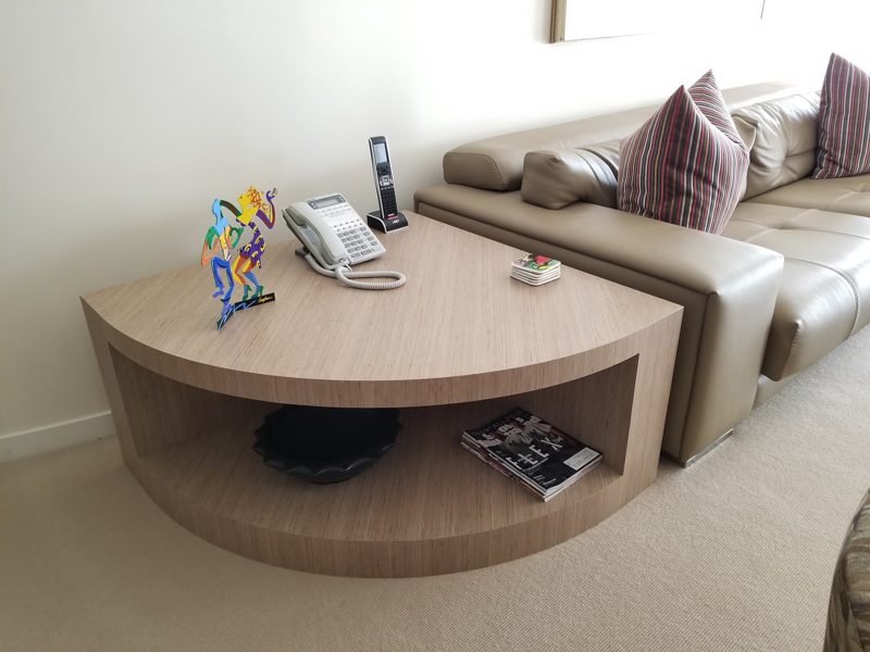 Light wood curved end table with an open shelf beside a sofa