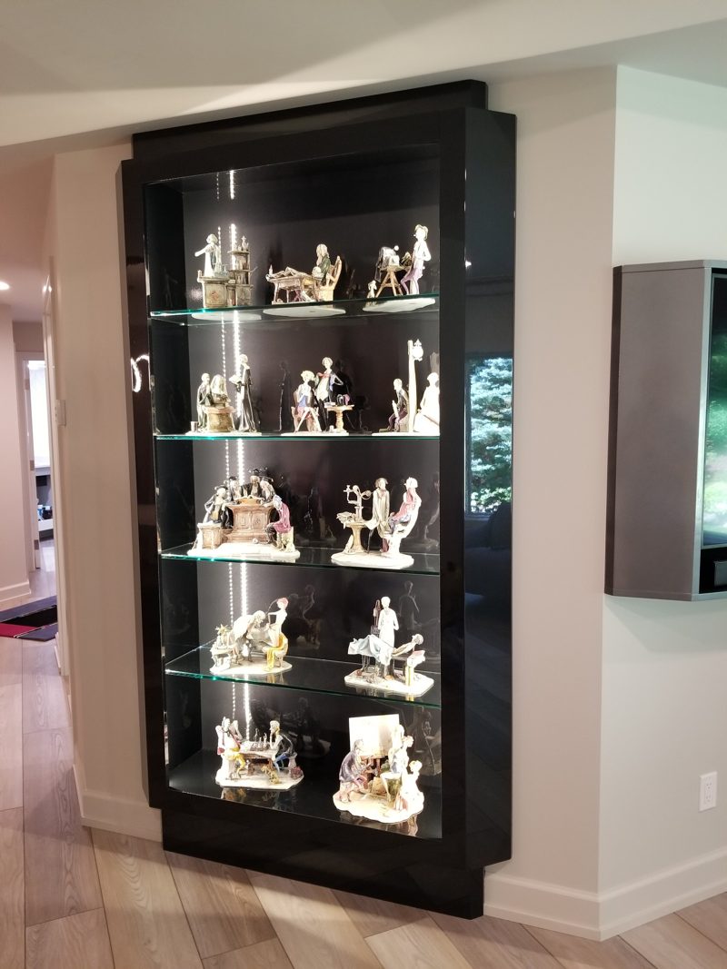Dark wood lit display case with glass shelves holding figurines