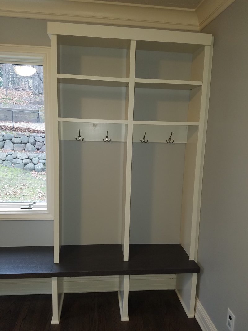 Angled view of white open lockers with coat hooks and a dark bench
