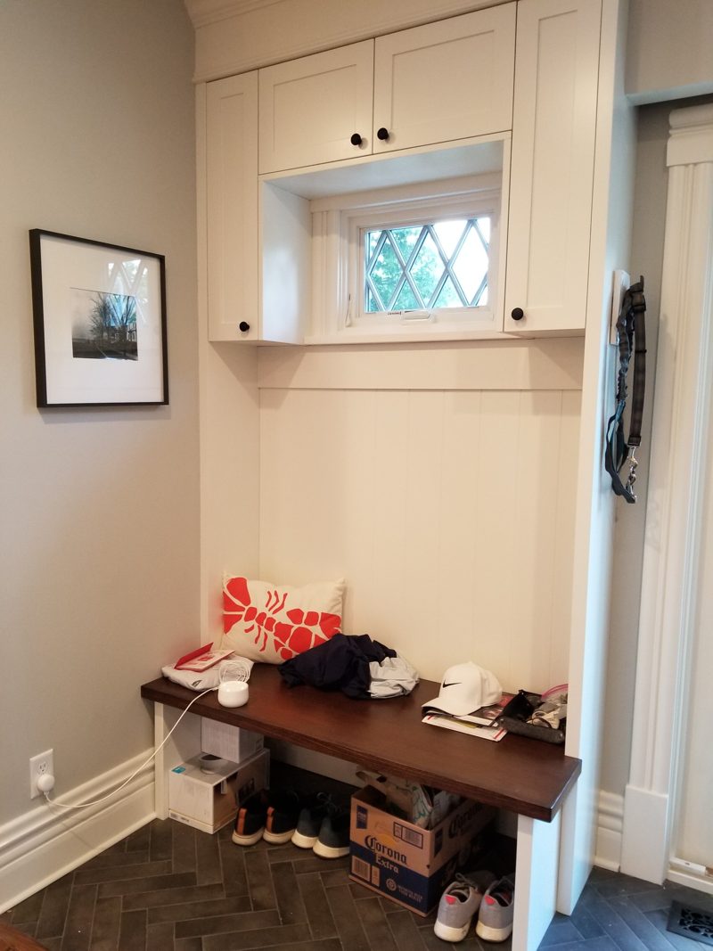 White entry cabinets above a small window and a dark wood bench with shoes