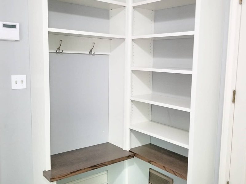 Close view of white corner shelves and hooks above dark wood benches