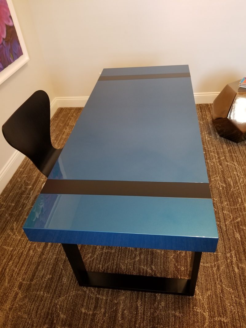 Glossy blue desk seen from the end with a dark stripe and base