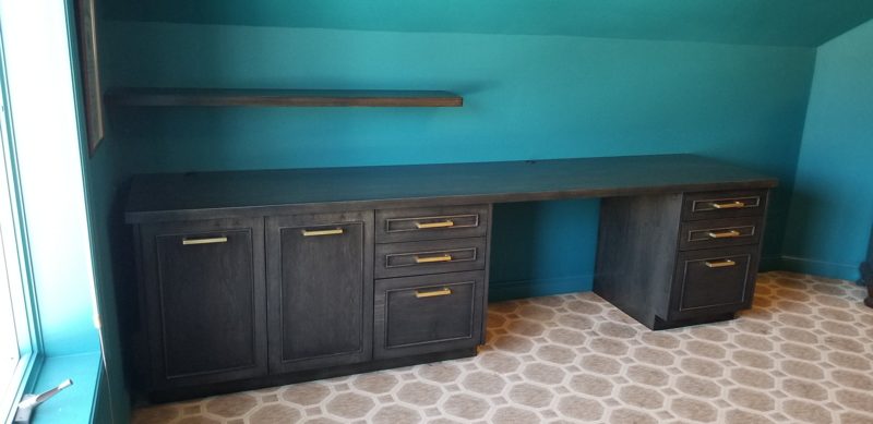 Dark gray built-in desk with filing drawers and a shelf in a teal room