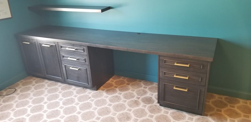 Gray-black built-in desk with drawers and brass pulls against a teal wall