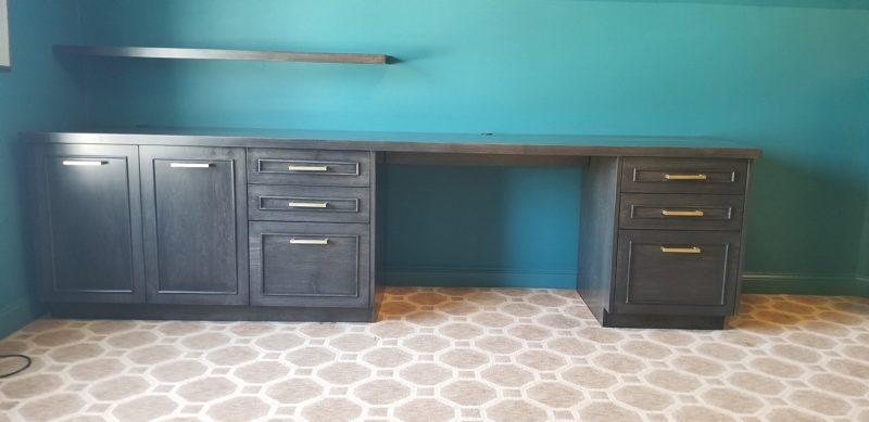 Long dark desk with two drawer banks and a floating shelf above