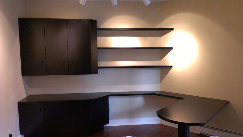 Black corner desk with a wall cabinet, floating shelves, and round table end