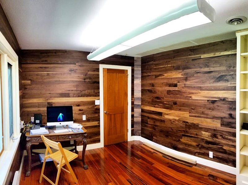Home office with dark wood plank walls, a small desk, and cherry floors