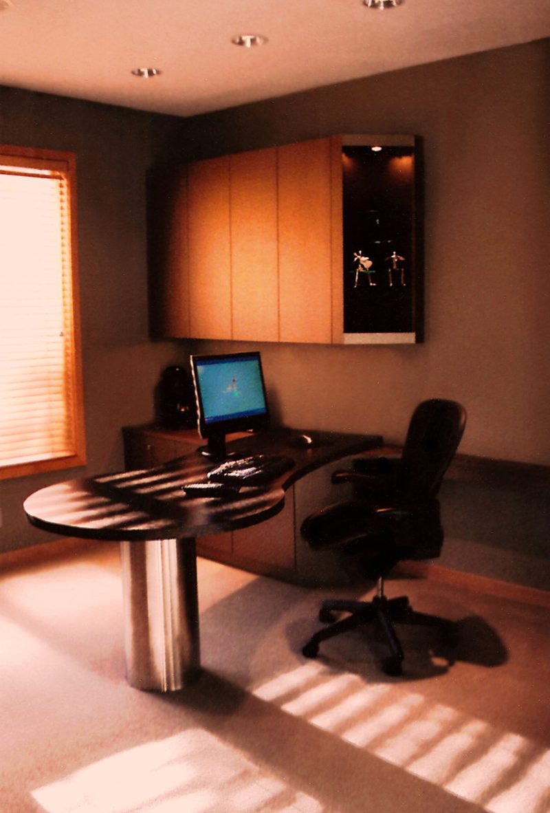Light wood wall cabinets above a desk with a round glass table